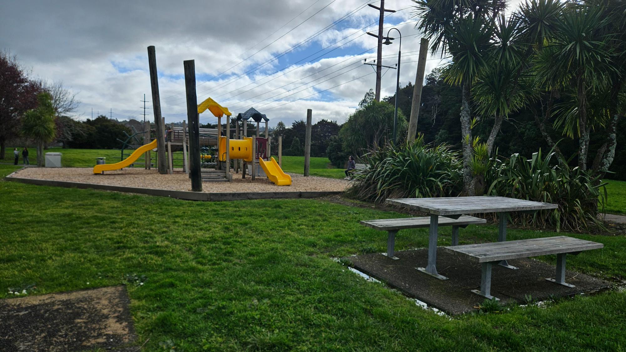 Two picnic tables sit beside the play area, with a wide grass field stretching out alongside the playground.