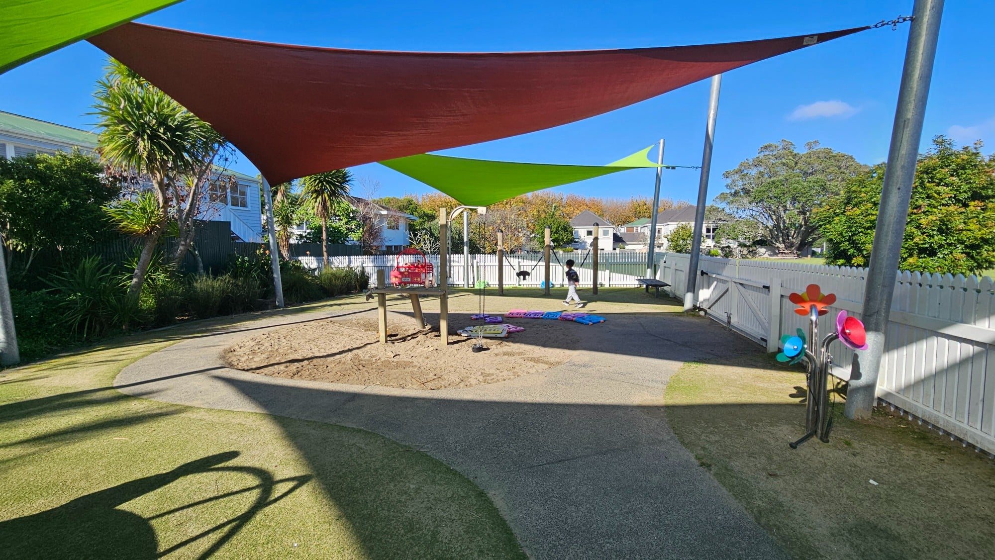 Shade sails and fully fenced play area — this long, narrow playground keeps most of the equipment under cover and enclosed